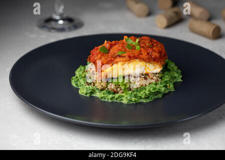 Gebratenes Stück Kabeljaufischfilet (Schellfisch) mit Quinoa, Karotte, Zwiebel, Tomaten und Sahne Spinat auf dunklen Tellern. Stockfoto