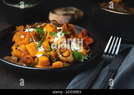 Salat mit gebackenem Kürbis, Thymian, gerösteten Zwiebeln und Joghurtsause, ein köstliches Herbstgericht. Auf dunklem Hintergrund. Selektiver Fokus Stockfoto