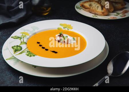 Kürbiscremesuppe mit Zwiebeln, Kräutern, Ricotta-Käse, Kürbisöl und gebratenem Baguette. Vegetarisches Essen. Stockfoto