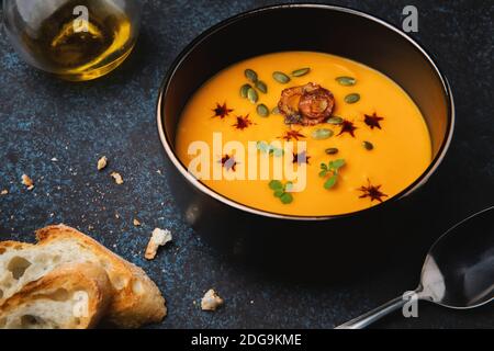 Kürbiscremesuppe mit Zwiebeln, Kräutern, Kürbiskernen, Kürbisöl und gebratenem Baguette. Vegetarisches Essen. Stockfoto