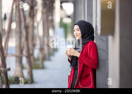 Moderne muslimische Frau, die mit einem Take-away über die Straße geht Kaffee Stockfoto