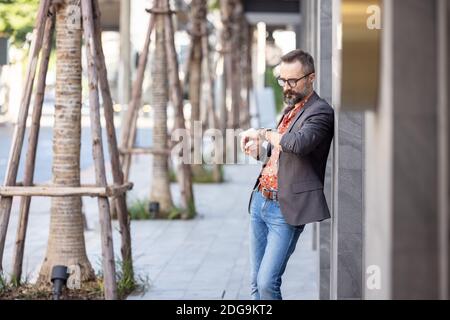 Attraktive junge Geschäftsmann in stilvollen Anzug Blick auf Uhr in Geschäftsviertel im Freien Stockfoto