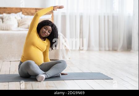 Fröhliche schwarze schwangere Frau macht Morgenübungen zu Hause Stockfoto