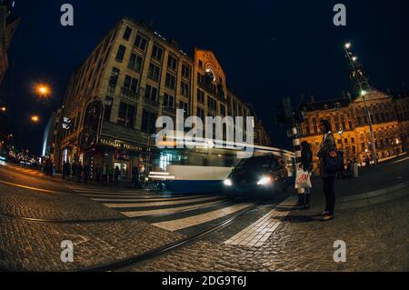 Straßenbahn und Auto überqueren Amsterdam Dam in den Niederlanden bei Nacht. Menschen warten darauf, die Straße vor Madame Tussaud zu überqueren. Stockfoto