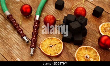 Shisha Hintergrund für Neujahr und weihnachten. Shisha, Holzkohle, trockene Orangenscheiben und weihnachtliche rote Kugeln auf einem Holzhintergrund Stockfoto