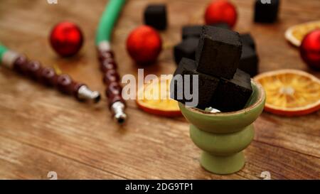 Shisha Hintergrund für Neujahr und weihnachten. Shisha, Holzkohle, trockene Orangenscheiben und weihnachtliche rote Kugeln auf einem Holzhintergrund Stockfoto