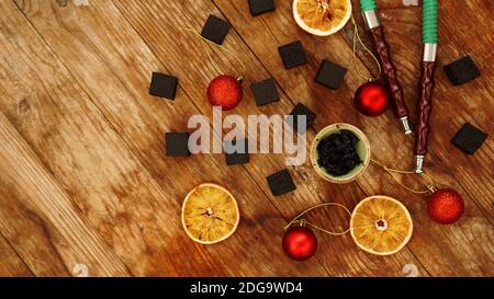 Shisha Hintergrund für Neujahr und weihnachten. Shisha, Holzkohle, trockene Orangenscheiben und weihnachtliche rote Kugeln auf einem Holzklößchen. Für Text platzieren - Ansicht von oben Stockfoto