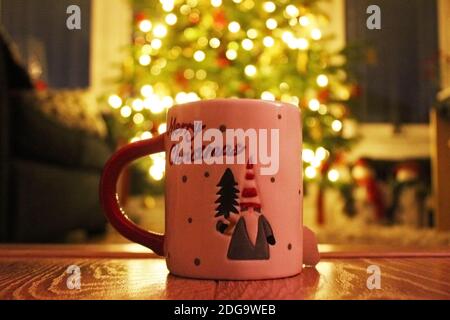 Nahaufnahme rot-weiß handbemalter Weihnachtsbecher auf einem Holzboden vor vergriffenen Weihnachtsbaumlichtern in Manchester, England Stockfoto