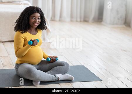 Lächelnde schwangere Frau trainieren mit Hanteln zu Hause Stockfoto