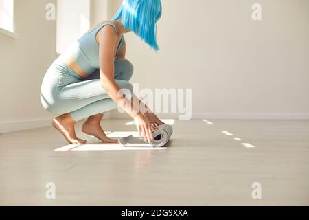 Junge sportliche Frau Rollen Yogamatte auf dem Boden am Morgen nach dem Training. Stockfoto