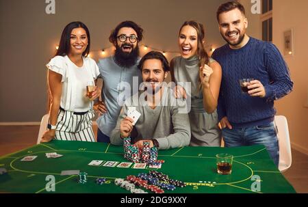 Gruppe junger lächelnder Freunde, die Spaß mit Spielbrett haben Spiele mit Karten und Chips zu Hause Stockfoto