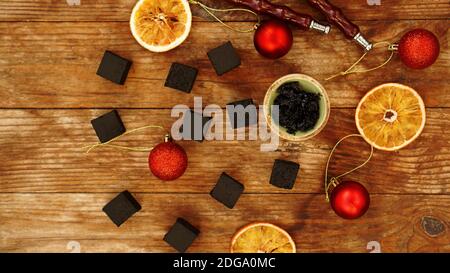 Shisha Hintergrund für Neujahr und weihnachten. Shisha, Holzkohle, trockene Orangenscheiben und weihnachtliche rote Kugeln auf einem Holzhintergrund. Draufsicht Stockfoto