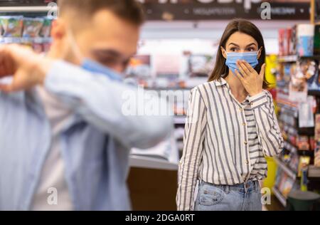 Kranker Mann Hustet In Elbow, Verängstigte Frau, Die Ihn Ansieht Stockfoto