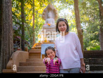 Tourist Asian Mutter und Tochter vor verschwommener weißer Buddha Skulptur und Baum im Wat Umong oder Umong Tempel von Chiang Mai, Thailand. Stockfoto