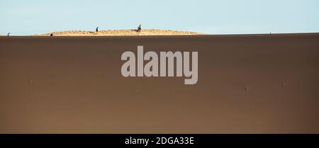 Touristen, die hinter einer riesigen Sanddüne im Valle de la Luna, Tal des Mondes, Atacama Wüste, Nordchile, Südamerika, in den Schatten gestellt wurden Stockfoto