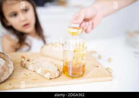 Männliche Hand pflücken Honig aus einem Glas neben einem Brotscheibe Stockfoto