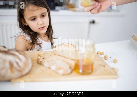 Männliche Hand pflücken Honig aus einem Glas neben einem Brotscheibe Stockfoto