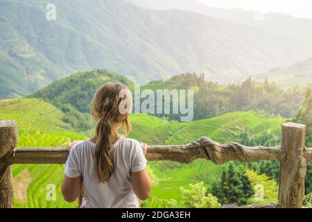 Niedliches junges Mädchen, das auf einem Aussichtspunkt der neun Drachen und fünf Tiger steht und die stufenförmigen Longji-Reisterrassen, Pingan Village, nördliches GUI, bewundert Stockfoto