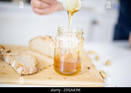 Männliche Hand pflücken Honig aus einem Glas neben einem Brotscheibe Stockfoto