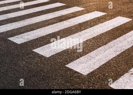 Ein leerer Fußgängerüberweg auf einer neuen Straße. Der Straßendienst zeichnete die Markierungen. Sonnenuntergangsgradient. Horizontales Foto. Stockfoto