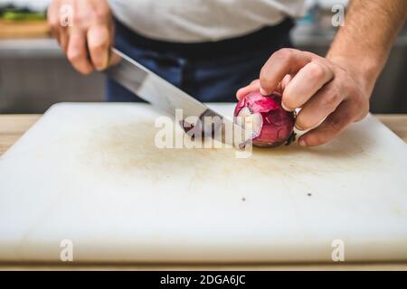 Koch schneidet rote Zwiebel auf dem Küchenbrett. Speisezubereitung im Restaurant Stockfoto