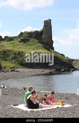 Dunure Castle, Dunure, Ayrshire, Schottland, Großbritannien. Dunure war der uralte Sitz der Familie Kennedy, die traditionell die Herren von Carrick und schließlich die Grafen von Cassillis waren.Ein Familienpicknick am steinigen Strand vor dem Schloss. Das Schloss und das Dorf werden im Outlander-Franchise genutzt Stockfoto