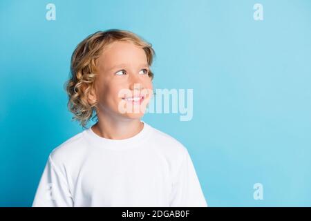 Foto von toothy lächelnden Jungen aussehen leeren Raum tragen weiß t-Shirt isoliert auf blauem Hintergrund Stockfoto