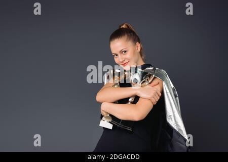 Glückliche Geschäftsfrau, Superheld mit zwei Trophäen in den Händen, zufrieden mit Ruhm auf einem grauen Hintergrund. Stockfoto