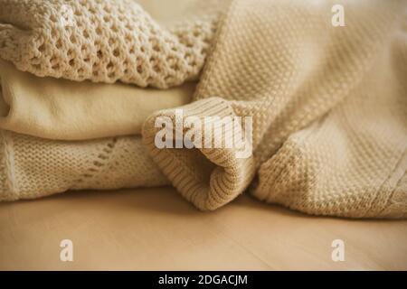 Beige Wollpullover liegen auf dem Bett, gefaltet in einem Flor, aus dem der Ärmel eines der Pullovern gefallen ist. Warme Kleidung für kalten Herbst und Stockfoto