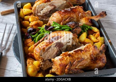 Ofengebackenes halbiertes Huhn mit Kartoffeln und Gemüse auf einem Backblech Stockfoto