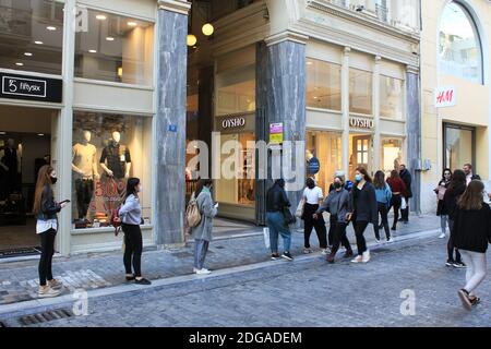 Nach der Ankündigung einer zweiten Sperre in Griechenland wegen des Ausbruchs von Covid-19 warten sich die Kunden an, um in Bekleidungsgeschäfte im Zentrum von Athen zu gelangen - Stockfoto