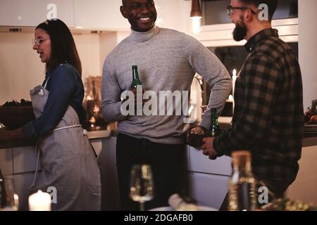 Zwei männliche Freunde lachen zusammen, während sie bei Getränken reden Eine Küche während einer Dinnerparty Stockfoto