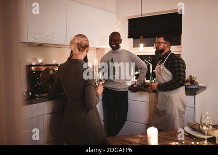 Eine Gruppe lächelnder Freunde, die in einer Küche miteinander sprechen Bei einem Drink vor einer Abendparty Stockfoto