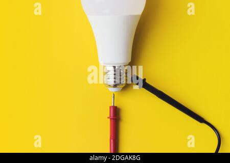 LED-Glühlampe mit Multimetersonden auf gelbem Hintergrund. Neue Technologie der Energie, Eco Power Konzept. Speicherplatz kopieren. Energiesparkonzept Stockfoto