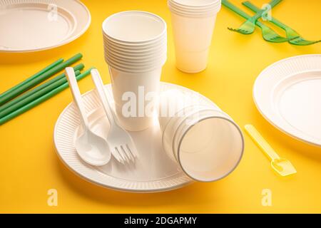Einweg-Geschirr aus Kunststoff. Gruppe von leeren Tellern, Tassen, Löffeln, Gabeln und Utensilien auf gelbem Tisch Stockfoto