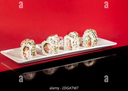 Sushi setzt Nigiri, Uramaki, California, Philadelphia, auf einen weißen Teller. Auf einem roten Hintergrund. Speicherplatz kopieren. Stockfoto
