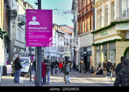 Heidelberg, Deutschland - Dezember 2020: Schilder für Gesichtsmaske und Entfernungsanforderungen in der deutschen Innenstadt von Heidelberg mit Menschen in der Einkaufsstraße i Stockfoto