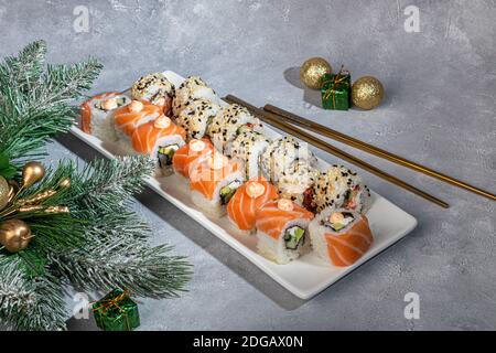 Sushi setzt Uramaki, California, Philadelphia, auf einen weißen Teller. Neujahr und festliches Konzept. Auf einem hellgrauen Hintergrund. Speicherplatz kopieren. Stockfoto