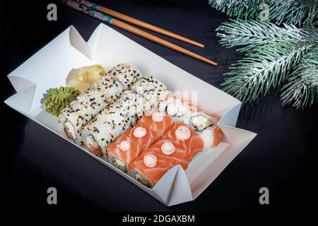 Sushi setzt Uramaki, California, Philadelphia, auf einen weißen Teller. Festliches Neujahrskonzept. Vor einem dunklen reflektierenden Hintergrund. Speicherplatz kopieren Stockfoto