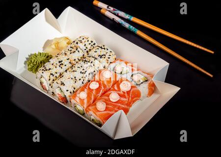 Sushi setzt Uramaki, California, Philadelphia, auf einen weißen Teller. Festliches Neujahrskonzept. Vor einem dunklen reflektierenden Hintergrund. Speicherplatz kopieren Stockfoto