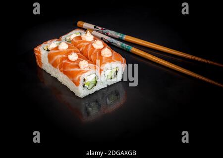 Sushi setzt Uramaki, California, Philadelphia, auf einen weißen Teller. Festliches Neujahrskonzept. Vor einem dunklen reflektierenden Hintergrund. Speicherplatz kopieren Stockfoto