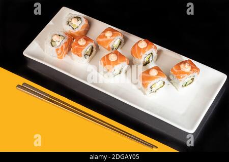 Sushi setzt Uramaki, California, Philadelphia, auf einen weißen Teller. Festliches Neujahrskonzept. Vor einem dunklen reflektierenden Hintergrund. Speicherplatz kopieren Stockfoto