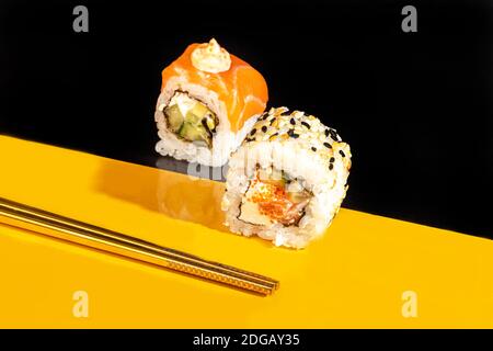 Sushi setzt Uramaki, California, Philadelphia, auf einen weißen Teller. Festliches Neujahrskonzept. Vor einem dunklen reflektierenden Hintergrund. Speicherplatz kopieren Stockfoto