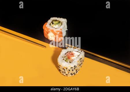 Sushi setzt Uramaki, California, Philadelphia, auf einen weißen Teller. Festliches Neujahrskonzept. Vor einem dunklen reflektierenden Hintergrund. Speicherplatz kopieren Stockfoto