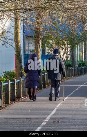 Ein älteres Paar, das zusammen auf einem Weg oder Bürgersteig geht der Mann, der einen Gehstock benutzt, um Hilfe und Hilfe beim Gehen zu erhalten. Stockfoto