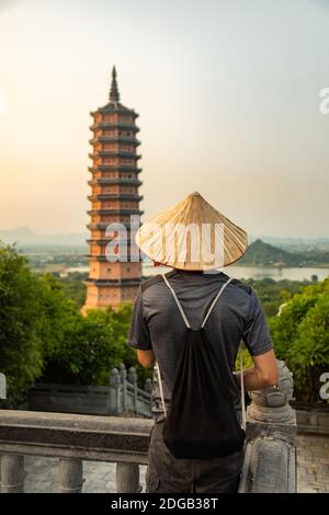 Ein Kerl mit im Hintergrund die Bai Dinh Pagode bei Sonnenuntergang, im größten buddhistischen Tempelkomplex von Vietnam, in Ninh Binh Provinz. Stockfoto