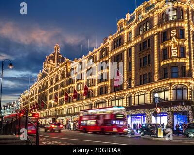 SALE Harrods Winterverkauf Lichter Sonnenuntergang Kaufhaus beleuchtet in der Abenddämmerung mit beleuchtetem „Sale“-Schild, Shopper rasen den roten Bus und vorbei an Taxis auf der roten Route Brompton Road Knightsbridge London SW1 Stockfoto