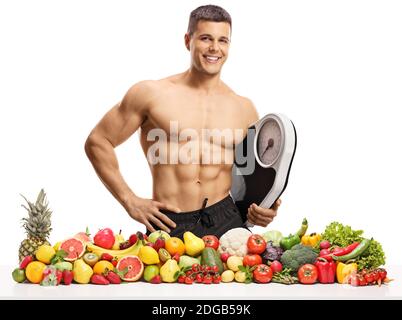 Fitness männliche Modell hält eine Messskala mit Früchten und Gemüse vor ihm isoliert auf weißem Hintergrund Stockfoto