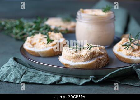 Sandwiches mit geräuchertem Lachs und weicher Frischkäse-Pastete oder Mousse mit Thymian und Rosmarin auf einer Keramikplatte, grüner Betonboden. Selektive Stockfoto