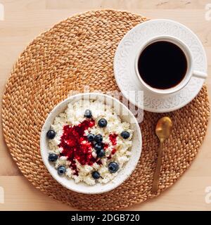 Weiße Schale mit hausgemachtem Quark mit Marmelade, Himbeeren, Heidelbeeren und einer Tasse Kaffee Stockfoto